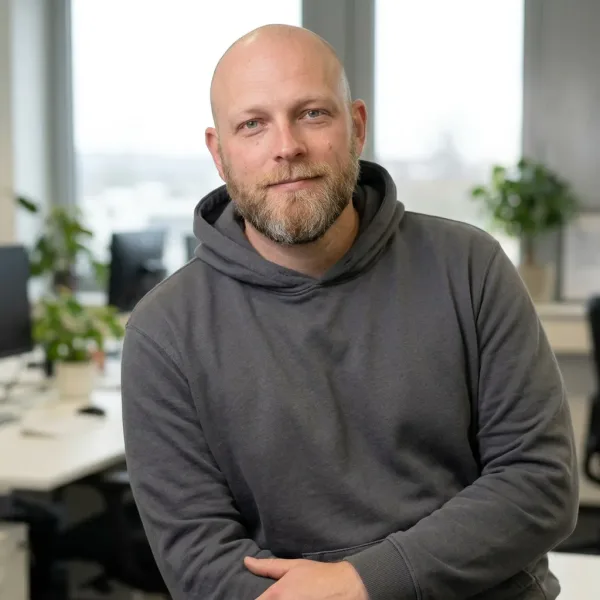 Mann mit Bart im Hoodie sitzt lächelnd in Büro mit Pflanzen. – Website Baukasten